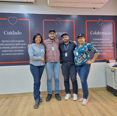 Foto de três docentes e uma funcionária em pé abraçados e sorrindo.